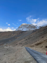 Obraz premium Scenic view of a mountain with snow on top and a road in the foreground near a rocky area on a clear day