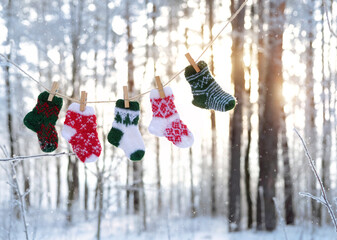 winter forest landscape with colorful knitted little wool socks hanging on rope, sunny nature background. symbol of festive winter season. Christmas, new year holidays atmosphere. cold snowy weather