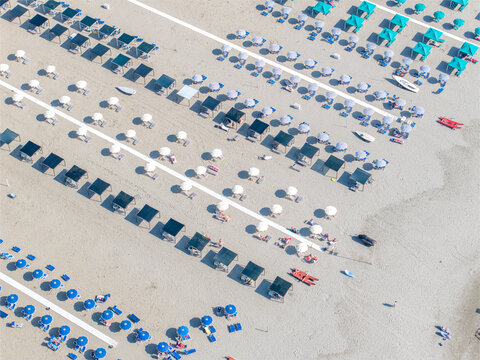Aerial view of ordered rows of sun umbrellas casting sharp shadows on the sandy beach, a vibrant contrast of turquoise and white against the warm sand, Forte dei Marmi, Tuscany, Italy.