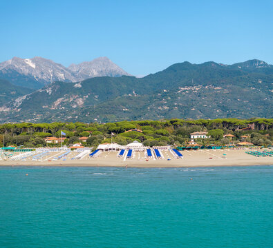Aerial view of the beach with its neat rows of umbrellas contrasting with the deep blue sea under a clear sky, framed by the distant mountains, Forte dei Marmi, Tuscany, Italy.