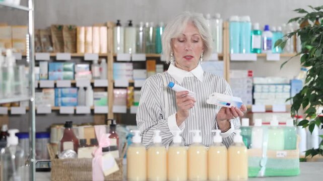 Elderly woman in summer clothes buys medicinal ointment at a pharmacy. High quality 4k footage
