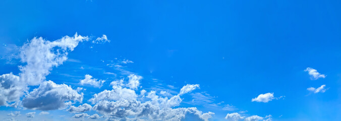 A panorama of cumulus clouds against a blue sky. A summery, serene landscape. The cloud's smooth movement copy space for banner text. Clear background with tiny white fluffy cloud.