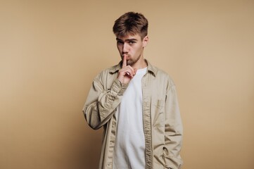 Fototapeta premium Young man making a shushing gesture with his finger on his lips in front of a plain background