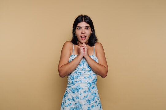 Surprised young woman shows excitement with hands clasped together in studio setting during indoor photo session