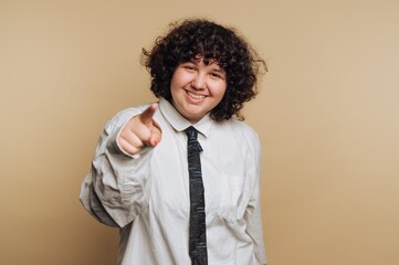 Person in light shirt and tie points at the viewer with a smile in a studio setting on a plain background