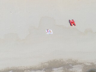 Aerial view of sun-kissed sands embrace the shore, with a striking red boat and a colorful sunbathing mat adding vibrant accents to the tranquil beach scene, Forte dei Marmi, Tuscany, Italy.