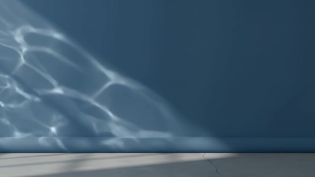 A serene and minimalist empty interior space features a clean, solid blue wall and a light gray concrete floor. Dynamic patterns of dappled, shimmering light, reminiscent of water reflections, dance g