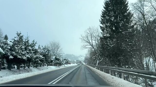 Timelapse of snowy winter road trip journey through picturesque landscape showcasing transition from urban to rural scenery with snow-covered trees lining road and vehicles navigating the winding path