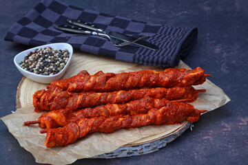 Grill torches. Slices of pork belly wrapped on skewers and served on a wooden board with spices.