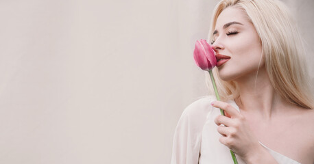 A blonde girl with long hair holding a bouquet of pink tulips against a light textured background. Happy International Women's Day, the first day of spring, Mother's Day, and spring holiday. banner