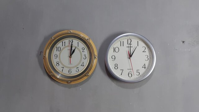 Footage of an analog quartz wall clock made in Japan, hanging on a gray painted wall.