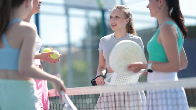 Team of female padel tennis players chatting during break on tennis court