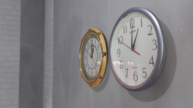 Footage of an analog quartz wall clock made in Japan, hanging on a gray painted wall.