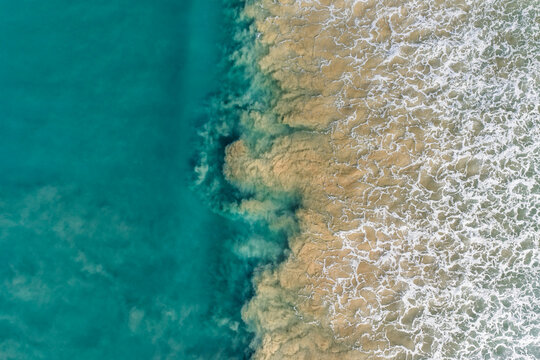Aerial view of the meeting of the turquoise sea and sandy shore creates a mesmerizing dance of color and texture along the Great Ocean Road, Lorne, Victoria, Australia.