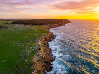 Aerial view of rugged cliffs meet the turquoise sea under a vibrant sunset sky, juxtaposing earthy tones with the ocean's cool hues, South Australia, Australia.