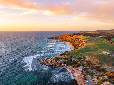 Aerial view of golden light kisses the rugged coastline where turquoise waves meet sandy beaches, revealing a vibrant contrast of nature's artistry, Port Willunga, South Australia, Australia.