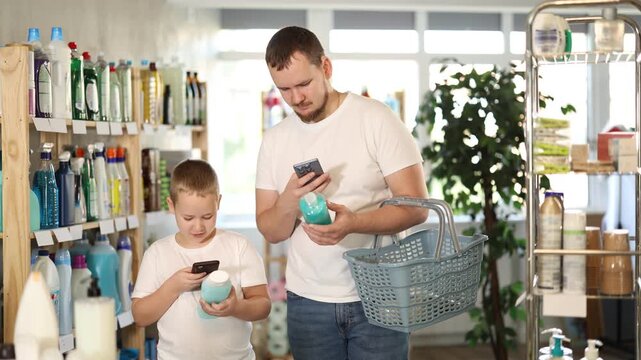  Young man with his son buyers scanning qr code for shampoo or shower gel in household chemicals store