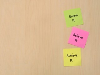 Colorful sticky notes with inspirational quotes Dream It, Believe It, Achieve It on a wooden background. Copy space 