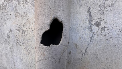 Hole in cracked concrete wall creating abstract urban texture background with damaged surface architectural decay concept on white background