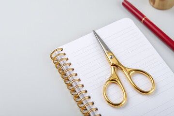 Gold Scissors On White Spiral Notebook With Red Pen On Light Grey Background
