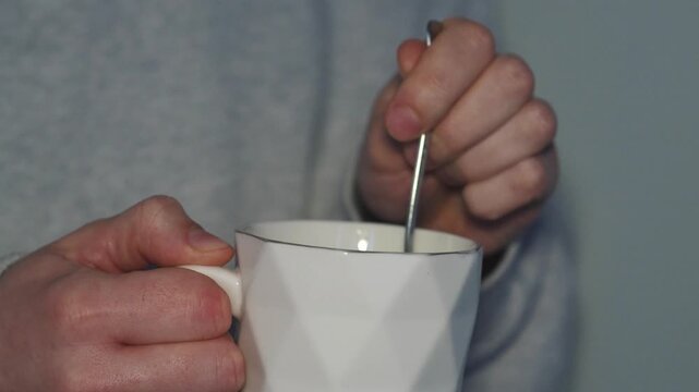A teacup and spoon in a glass.
Hot tea in a glass.
A man warms himself holding a cup of hot tea in his hands.