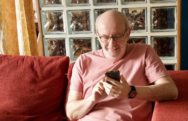 Senior man smiling using smartphone on couch