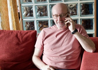 Senior man smiling enjoying smartphone call on sofa