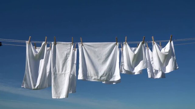 White clothes hanging on clothesline drying in fresh air under clear blue sky.
