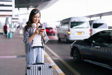 Asian woman traveler using smartphone with luggage at airport terminal