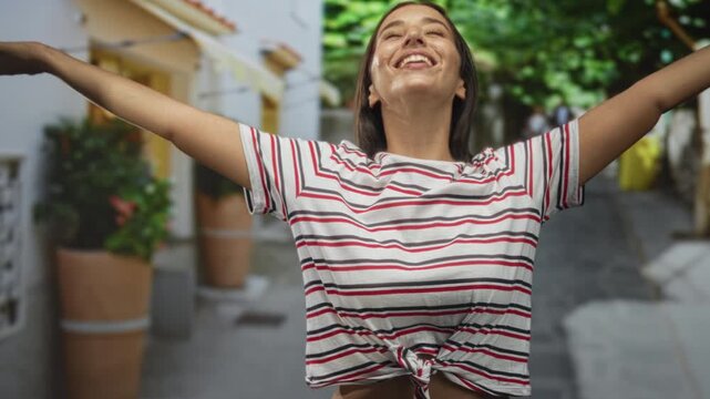 Young woman smiling with arms out, knotted striped shirt and exposed midriff on street; joy travel moment.