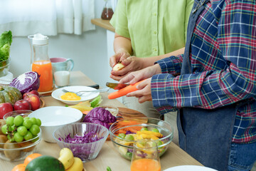 Closeup senior mother adult daughter preparing salad with fresh fruits vegetables on table, showing...