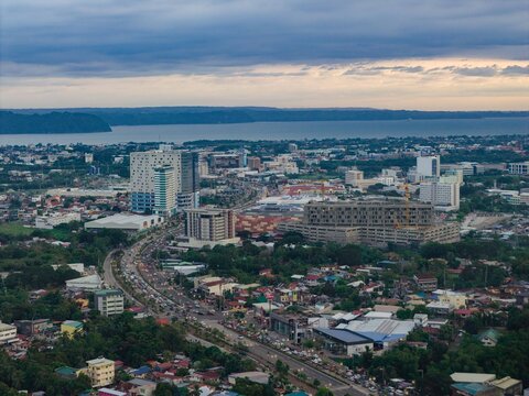 Aerial view of a bustling city with modern buildings nestled amidst lush greenery, and a calm sea in the distance, Iloilo City, Western Visayas, Philippines.
