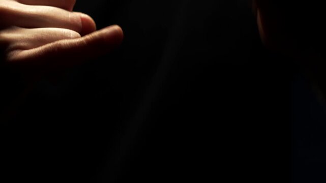 Pinky finger on a black background.
A man wiggles his pinky finger on his hand against a dark background from behind.
A man's hand and fingers