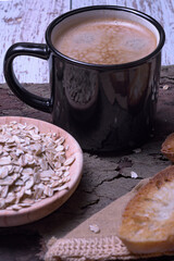 Black mug with coffee foam on tree bark, with a bowl of rolled oats and crispy toasted bread, rustic style
