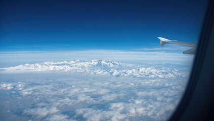 Fototapeta premium Aerial view of snow-covered Alps through airplane window, highlighting mountain landscape against blue sky, International Mountain Day