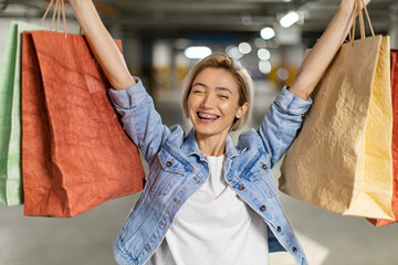 A joyful woman raises shopping bags in celebration, expressing excitement after a successful...