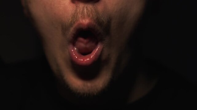Expression with tongue in mouth.
A man opens his mouth and shows his tongue sticking out against a dark background.