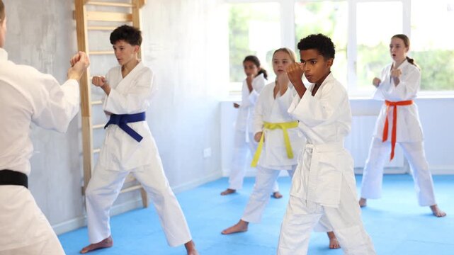 Group of preteen children of different nationalities in kimono trying new martial moves at karate class