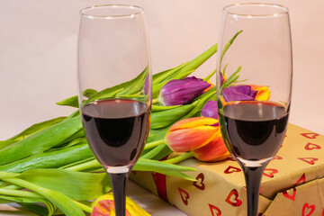 two glasses of red wine and a heart-patterned gift box nestled among fresh colorful tulips.