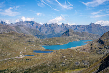 Lago Bianco reservoir stands majestically at Bernina Pass in Switzerland. Surrounded by towering alpine mountains, the tranquil lake reflects the stunning landscape under a clear sky.