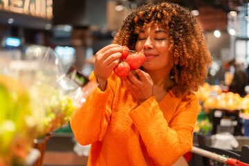 Woman enjoying fresh produce, smelling ripe tomatoes for healthy grocery shopping