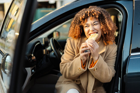 Woman enjoying a quick meal in her car, having a fast food snack on the go