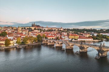 A serene morning scene captures Prague Castle rising above the city, with Charles Bridge stretching over the Vltava River. The old town awakens with soft light and vibrant rooftops.