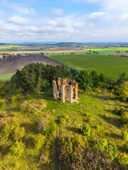 The drone captures the remains of the Chapel of the Exaltation of the Holy Cross in Bristev, surrounded by lush greenery and farmlands under a clear blue sky, showcasing nature reclaiming history.