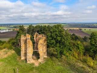 The ruins of the Chapel of the Exaltation of the Holy Cross stand amidst lush greenery in Bristev, captured from above by a drone on a clear day. Scenic fields stretch in the background.