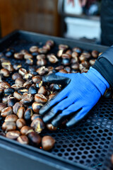 mano de persona moviendo las casta&ntilde;as asadas en u puesto de casta&ntilde;a