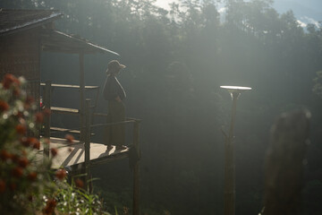 Naklejka premium Silhouette of a person resting on a wooden balcony overlooking misty mountains