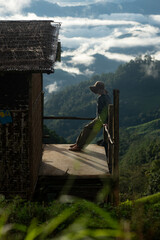Naklejka premium Silhouette of a person resting on a wooden balcony overlooking misty mountains