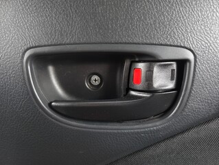 Interior car door handle with manual lock switch showing red indicator on textured black panel.