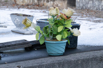 Artificial rose bouquet in a teal pot on a grave during winter